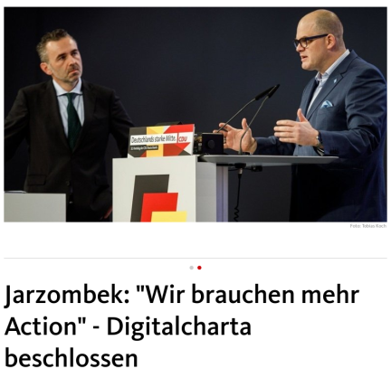 The image shows Thomas Jarzombe on the left, and Prof Dr. Jörg-Müller-Lietzkow on the right, a picture above a headline.saying: 'Wir brauchen mehr action" - DIgitalcharta beschlossen.